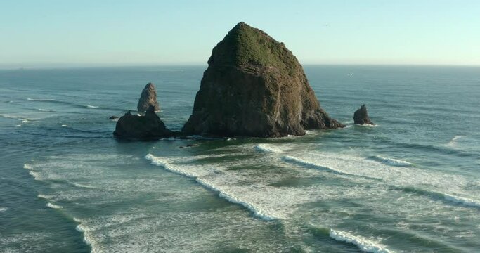 Orbiting shot of Haystack rock as seagulls dive towards the water.