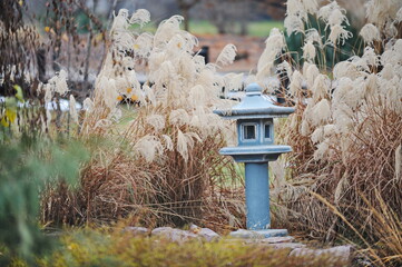 Japanese-style stone lantern among various plants in the botanical garden