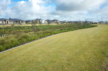 Nature reserve with green grass lawn and wetlands near a new suburban neighborhood. Public parkland with some Australian modern residential houses in the distance. Melbourne, VIC Australia.