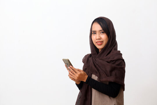 Portrait of happy asian muslim woman wearing a veil or hijab using a cell phone and smiling. Receiving good news, modern communication concept. Isolated on white background with copy space