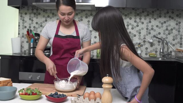 Asian mother teach little daughter making homemade pancake in mixing bowl for breakfast in the kitchen. Mom and child girl kid enjoy and having fun family weekend activity cooking together at home