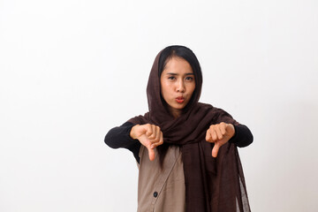 Portrait of asian muslim woman wearing a veil or hijab with thumbs down gesture, disappointed expression. Isolated on white background with copy space