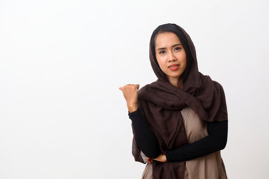 A portrait of happy asian muslim woman wearing a veil or hijab poiting or presenting something beside her. Isolated on white background with copy space
