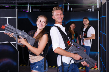 Excited team of laser tag winners guy and girl with laser pistols and losers team in background