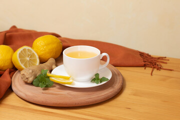 Ginger tea with mint and lemon. Healthy and hot drink. White cup on wooden board on wooden table. Selective focus.