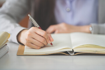 Stock photo of a young teenage woman Asian college student in student uniform studying and writing on a notebook in a university classroom