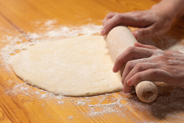 Hands with rolling-pin make dough for pizza. Italian pizza cooking preparation process on wood table. Pizza dough