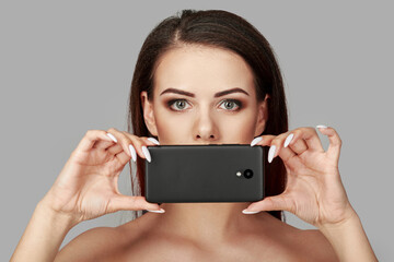 Portrait of attractive woman with bright makeup covering her mouth with smartphone