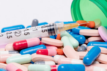 Medical pills and tablets spilling out of a drug bottle with syringe.