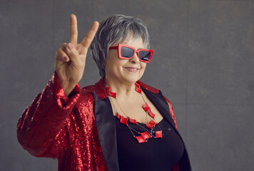 Happy grandma in red and black sequin party outfit and cool glasses smiling and doing victory...