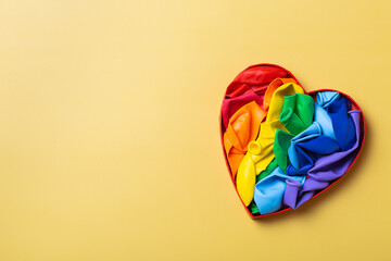 Heart shaped rainbow lgbtq flag against yellow background, pride month