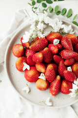 fresh strawberries on plate and small white flowers as decor. healthy food. raw food diet. food content. seasonal berries. selective focus