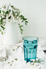 acacia flowers broth in blue glassware cup on cement background with lush flowering white acacia tree Branch , home self-treatment, useful properties of plants