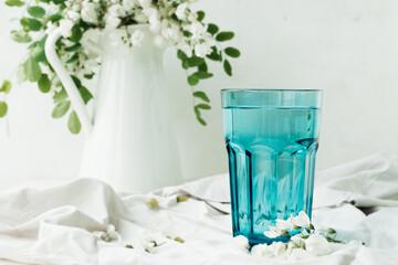 acacia flowers broth in blue glassware cup on cement background with lush flowering white acacia tree Branch , home self-treatment, useful properties of plants