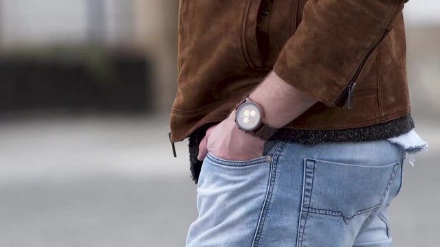 Man wearing a wooden wristwatch with hands in pockets walking,close up.