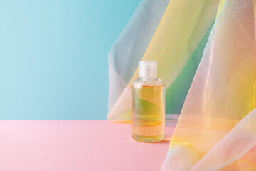 Hydrophilic cleanser oil on blue pink background with colorful rainbow organza fabric drapery....