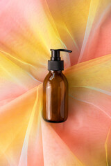 Bottle with pump for beauty product on colorful rainbow organza fabric. Mock-up container with...