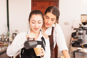 Focusing on half-body angle of Asian barista women fill milk into takeaway hot coffee cup while caucasian barista woman closely cheering her