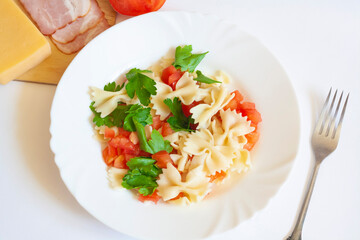 Pasta farfalle with tomatoes and herbs in a plate, fork, bacon, cheese and tomato on a white background, flat lay