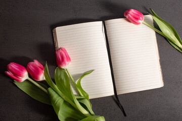 red tulips and notebook on dark background.