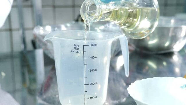 Pouring olive oil into empty measuring bowl. Food processing plant. Cooking dough n modern foodstuff manufacturing. 4 k video