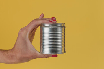 female hand holding can of food on yellow background