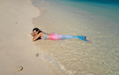 happy Asian woman in mermaid bikini swimwear lay down on clear blue sea beach