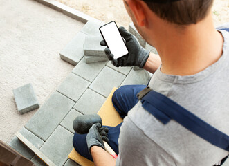 bricklayer holding the phone with blank screen in hand on gloves.  mockup for house repair or...