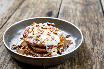 American pancakes with nuts, maple syrup and coconut cream on wooden table. Tasty sweet food for breakfast, brunch or lunch in outdoor cafe or restaurant