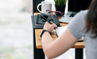 Cropped shot of woman hand holding pen and writing on notebook while sitting at the table.