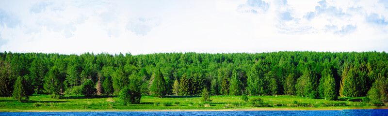 Landscape panoramic banner with a beautiful view of the bank of the blue Volga River with green forest and sky in Russia. Summertime landscape banner, panorama with copy space for text.