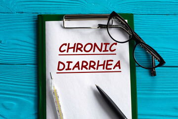 CHRONIC DIARRHEA - word in a notepad on a blue background with a pen, glasses and a thermometer