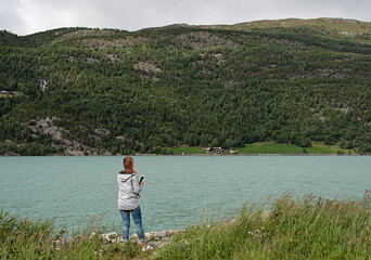 Fototapeta na wymiar Woman photographs the turquoise lake. The color is caused by algae from melting snow in the mountain