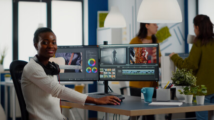 African video editor looking at camera smiling editing video project in post production software working in creative studio office. Videographer editing audio film montage on professional computer