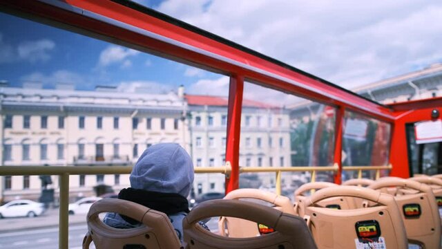 A hooded man sits on a red tour bus and takes pictures of the city on his phone. Walk through the most beautiful city in Russia.