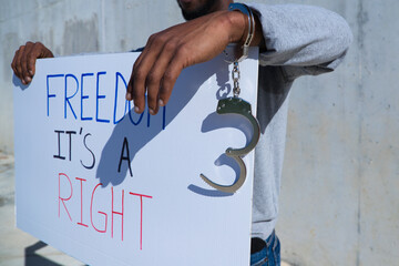African-american man holds up a banner that reads freedom is a right. The man holds a shackle or...