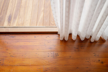 White curtains on the windows and the wooden floor in the room at home.