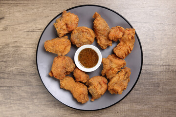Light battered deep fried chicken variety mix pieces pile flaky meat on grey plate honey garlic clear sauce in center over wooden background