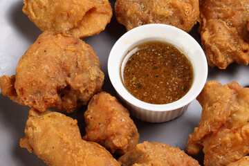 Light battered deep fried chicken variety mix pieces pile flaky meat on grey plate honey garlic clear sauce in center over wooden background
