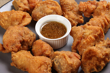 Light battered deep fried chicken variety mix pieces pile flaky meat on grey plate honey garlic clear sauce in center over wooden background