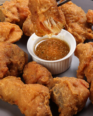 Light battered deep fried chicken variety mix pieces pile flaky meat on grey plate on fork dripping honey garlic clear sauce in center over wooden background