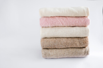 Fototapeta na wymiar cozy milky beige and white natural wool sweaters, folded on a white background close-up. clothes made of merino wool, alpaca, natural eco-fabrics. the concept of conscious consumption. flat lay
