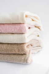 cozy milky beige and white natural wool sweaters, folded on a white background close-up. clothes made of merino wool, alpaca, natural eco-fabrics. the concept of conscious consumption. flat lay