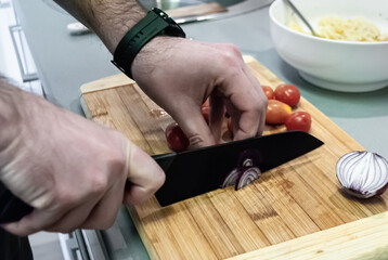 Man's hands cutting onions on a wooden board in the kitchen