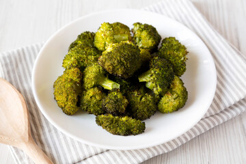 Homemade Roasted Broccoli with Salt and Pepper on a plate on a white wooden background, side view.