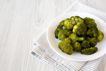 Homemade Roasted Broccoli with Salt and Pepper on a plate on a white wooden surface, side view. Copy space.