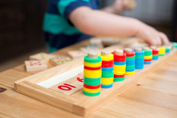 Fototapeta na wymiar infant child playing with different color wooden rings. engaged baby face. fine motor skills, therapy task for education and brain exercise. counting math play game.