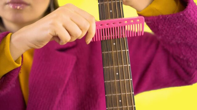 Female Hands With A Pink Comb Combing A Guitar, Surrealism On A Yellow Background, Close-up. Advertising Concept, Guitar Tuning, Psycho