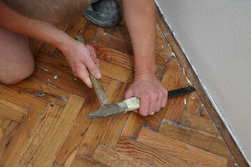 Closeup of worker hands removing old damaged parquet using chisel and hammer tools
