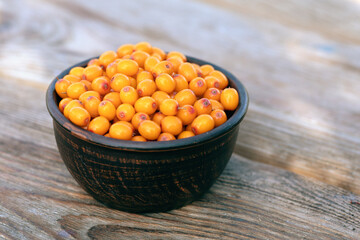 Fresh orange sea buckthorn berries in brown bowl on wooden background. Summer breakfast outside in country.